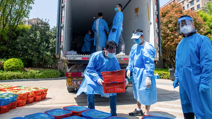 Community volunteers deliver vegetables to be distributed to residents in a compound during a Covid-19 lockdown in Shanghai on April 12, 2022. (Image: Liu Jin/Getty).